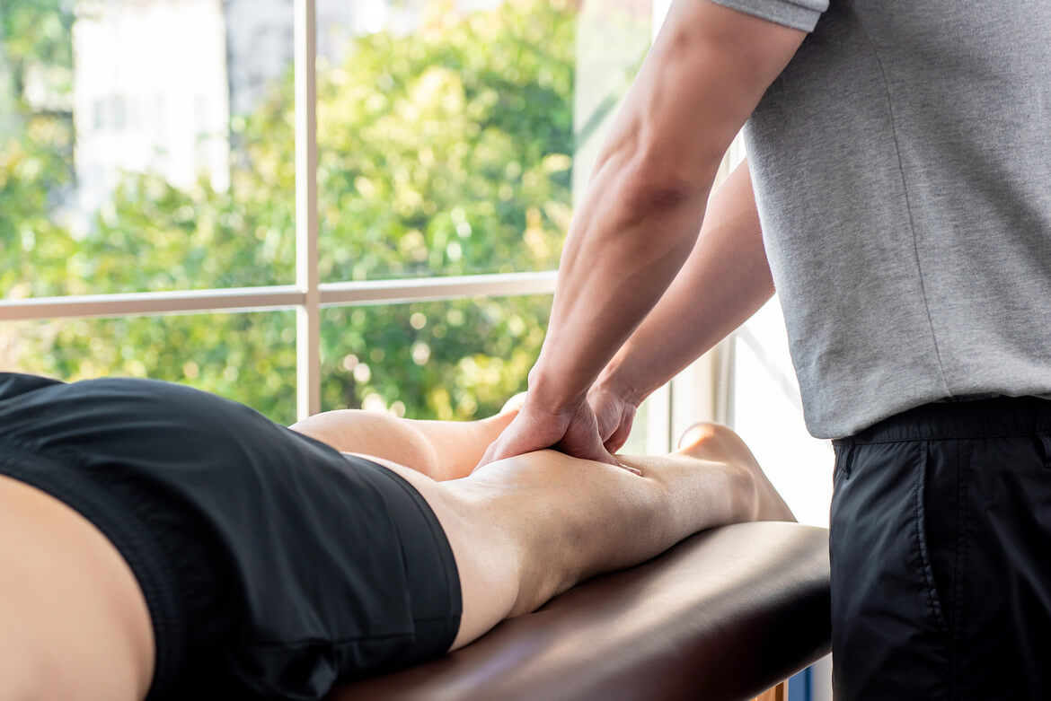 Male therapist giving leg massage to athlete patient on the bed in clinic, sports physical therapy concept